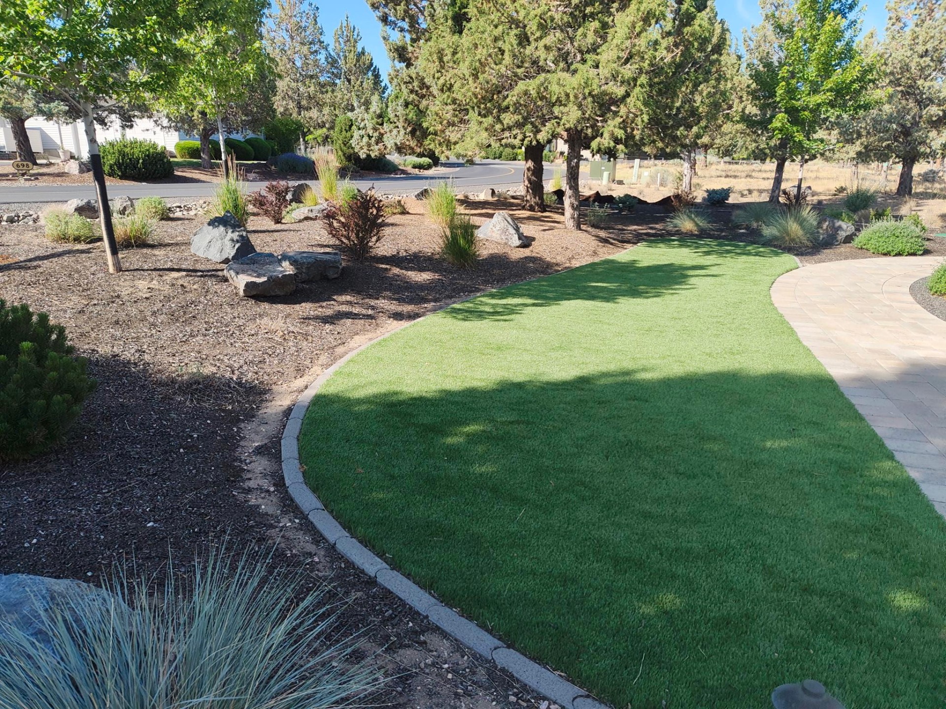 Artificial turf lawn installation with curved paver path and mulch beds at a Bend Oregon residence in Bend, OR by A1 Lawn & Landscape of Bend